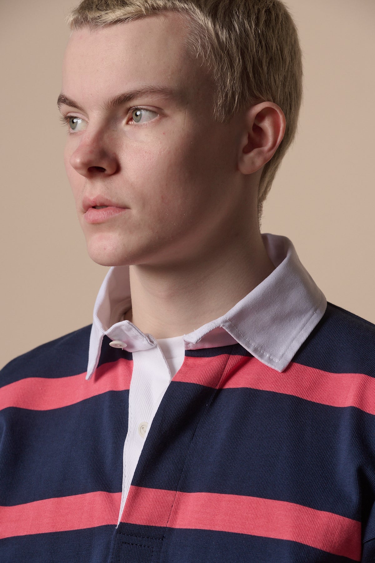 Portrait of blonde male wearing rugby shirt in navy pink with white collar unbuttoned over white t shirt