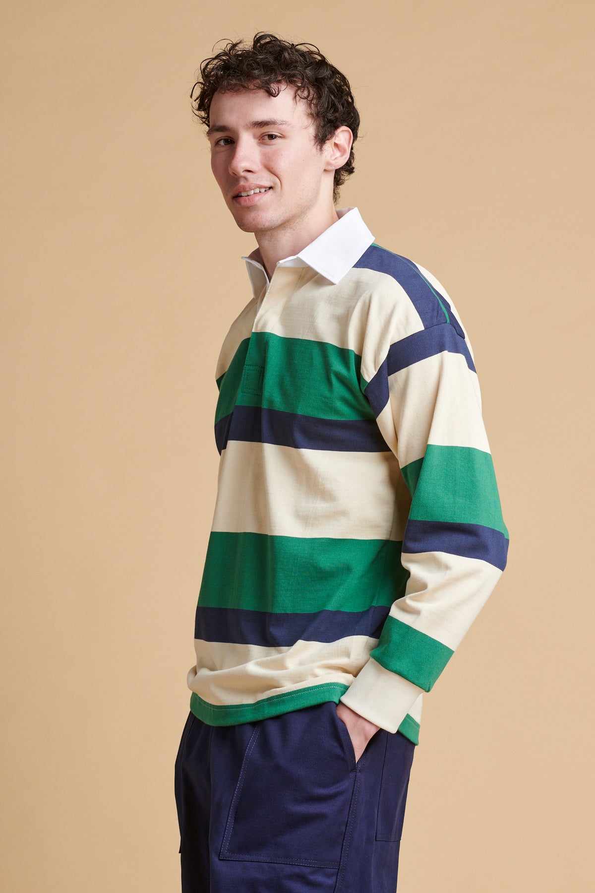 Male wearing striped rugby shirt in ecru navy bottle green.