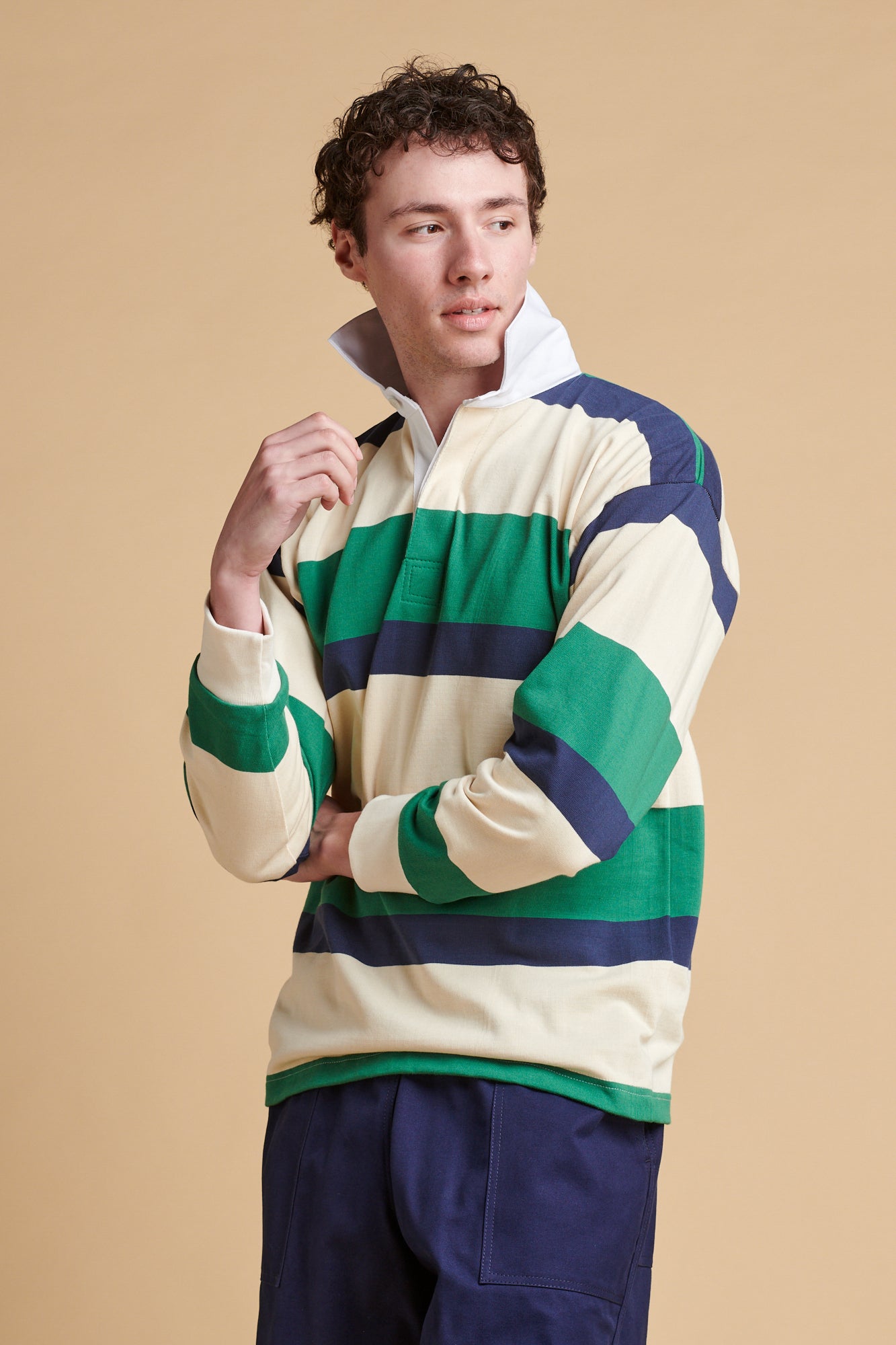 Male wearing striped rugby shirt in ecru navy and bottle green.