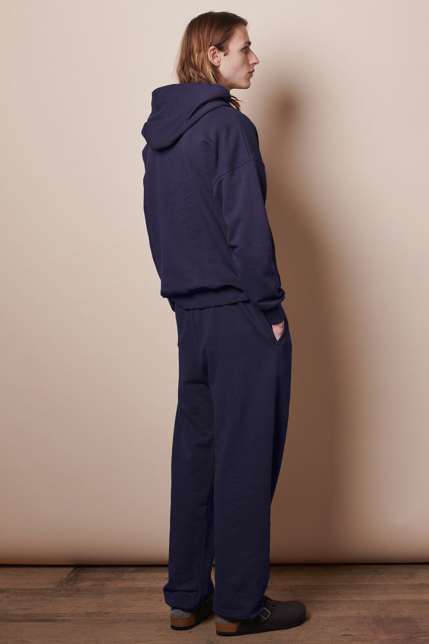 Full body image showing the back of male wearing men's sweatpants in navy paired with matching navy hooded sweatshirt