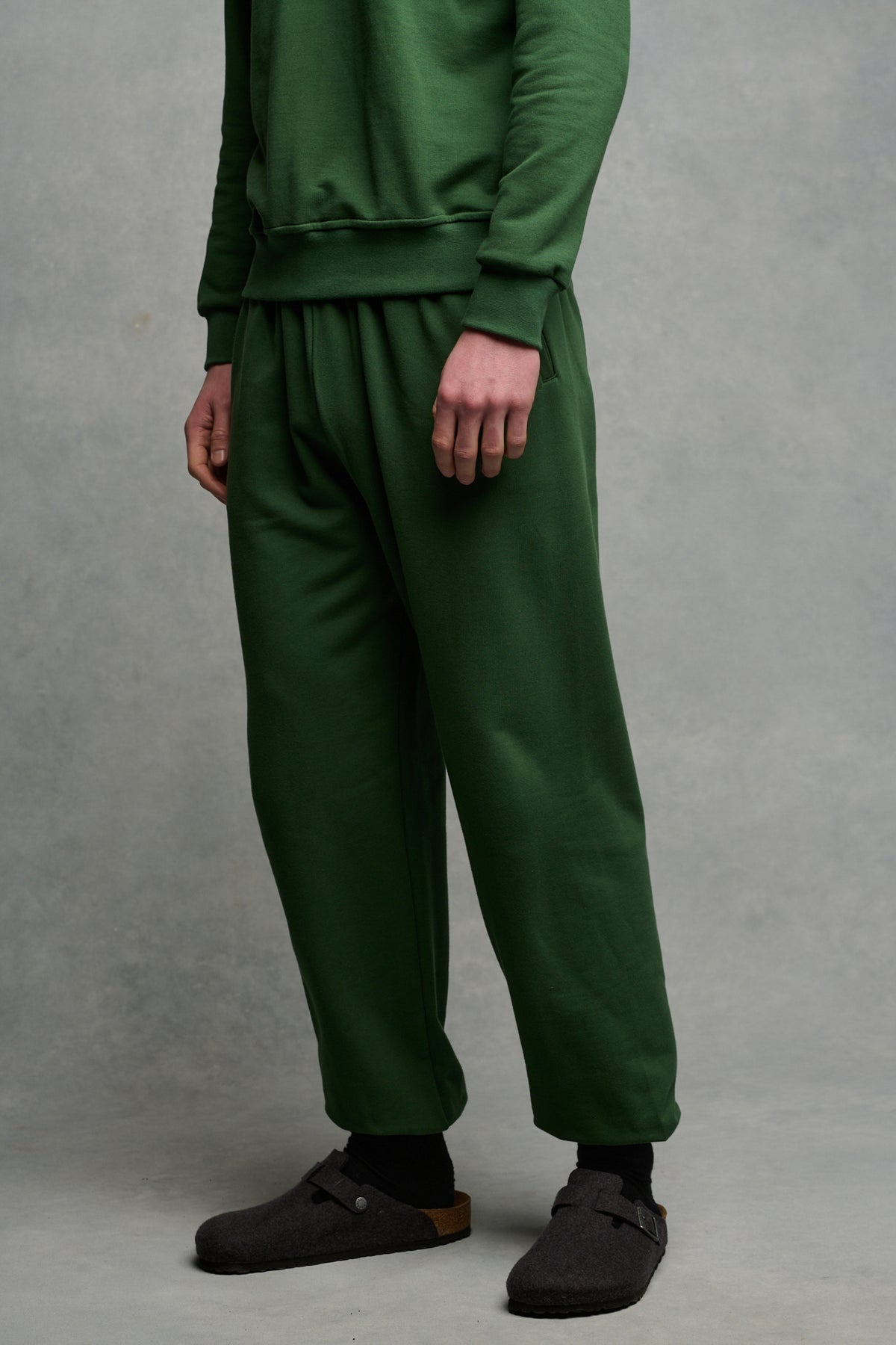 chest down image of male wearing sweatpants in bottle green paired with matching raglan sweatshirt in bottle green and Birkenstock Boston clog