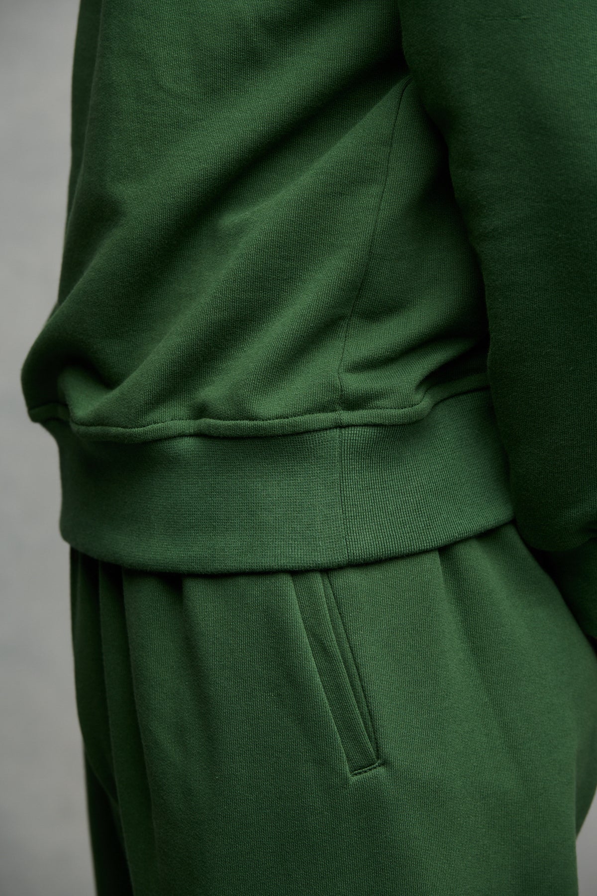 Close up image of men's sweatpants in bottle green, pocket detail and the hem of raglan sweatshirt.