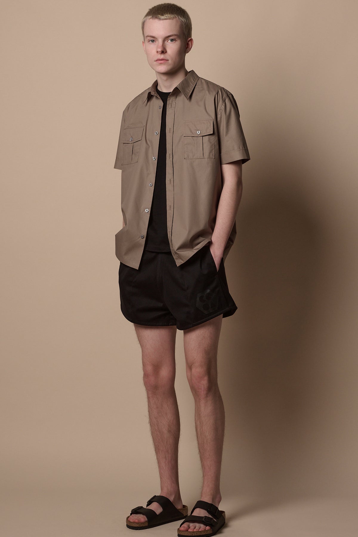 
            Full body image of male wearing unbuttoned Tom short sleeve military shirt in khaki open over crew neck t shirt in black paired with heavyweight sports short in black