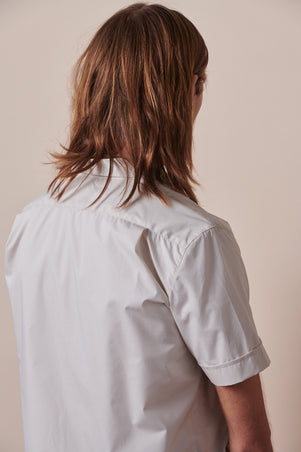 Back of male with shoulder length hair wearing Tom short sleeve military shirt in stone 