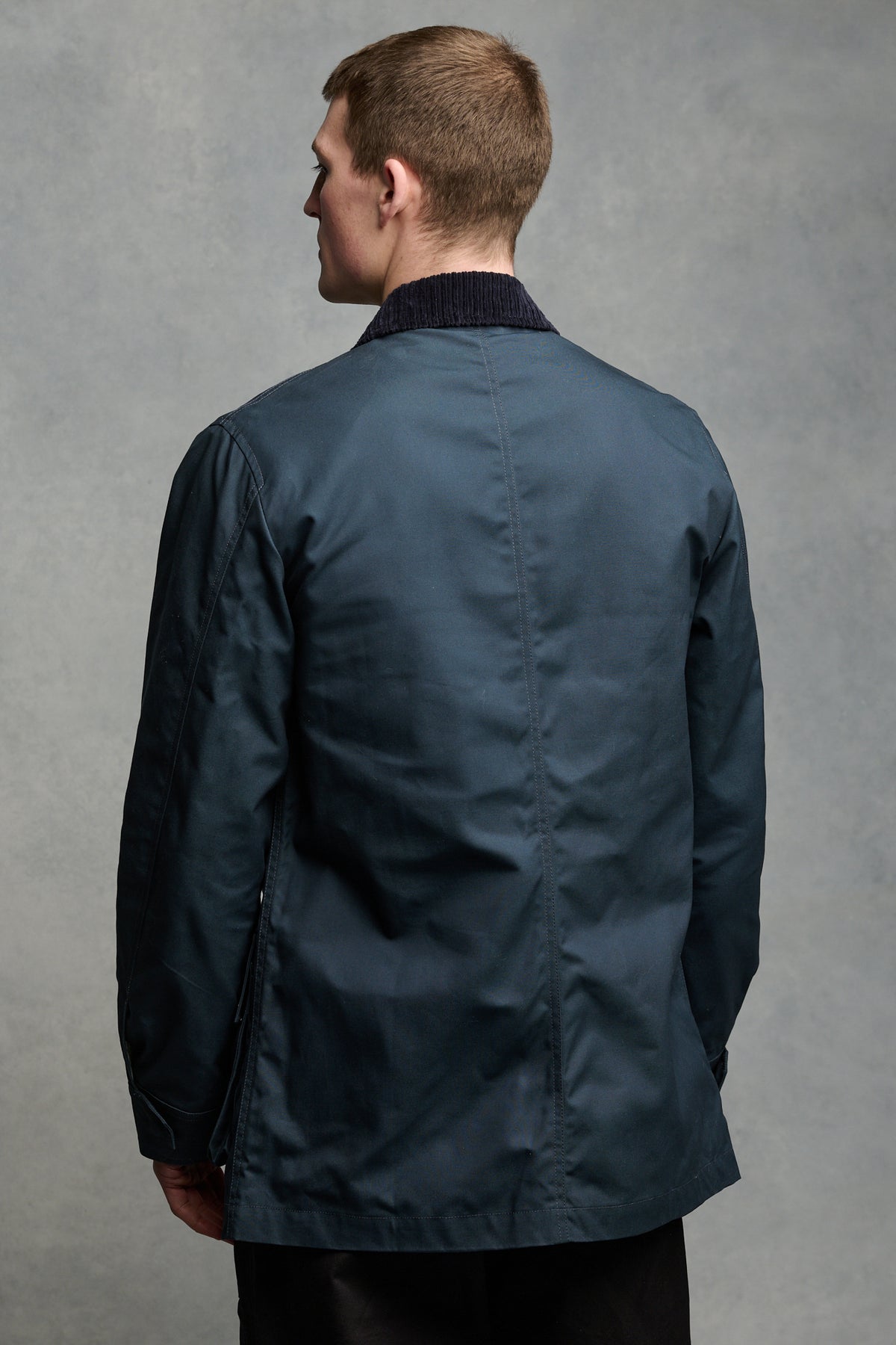 Thigh up image of the back of brunet male wearing barn jacket in navy.