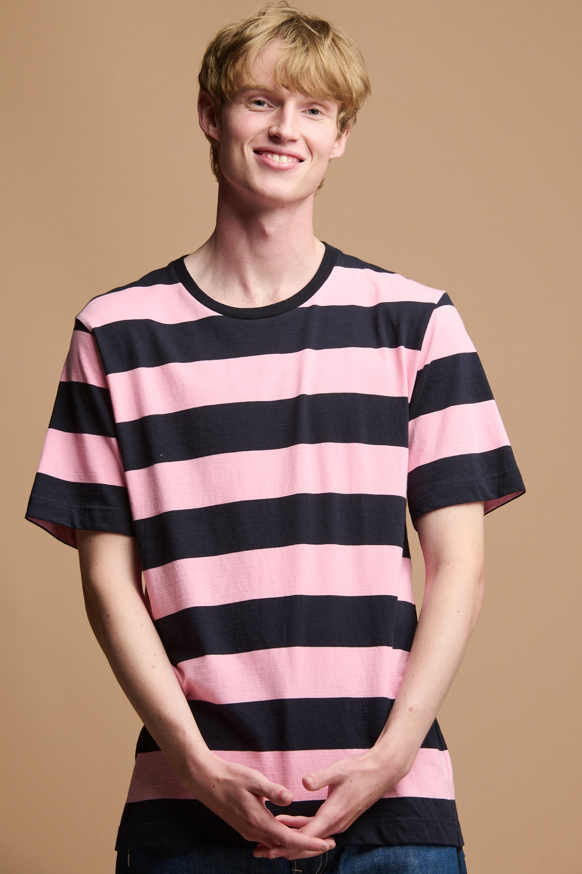 Thigh up image of smiley male wearing wide stripe short sleeve t shirt in navy blue and pink stripe