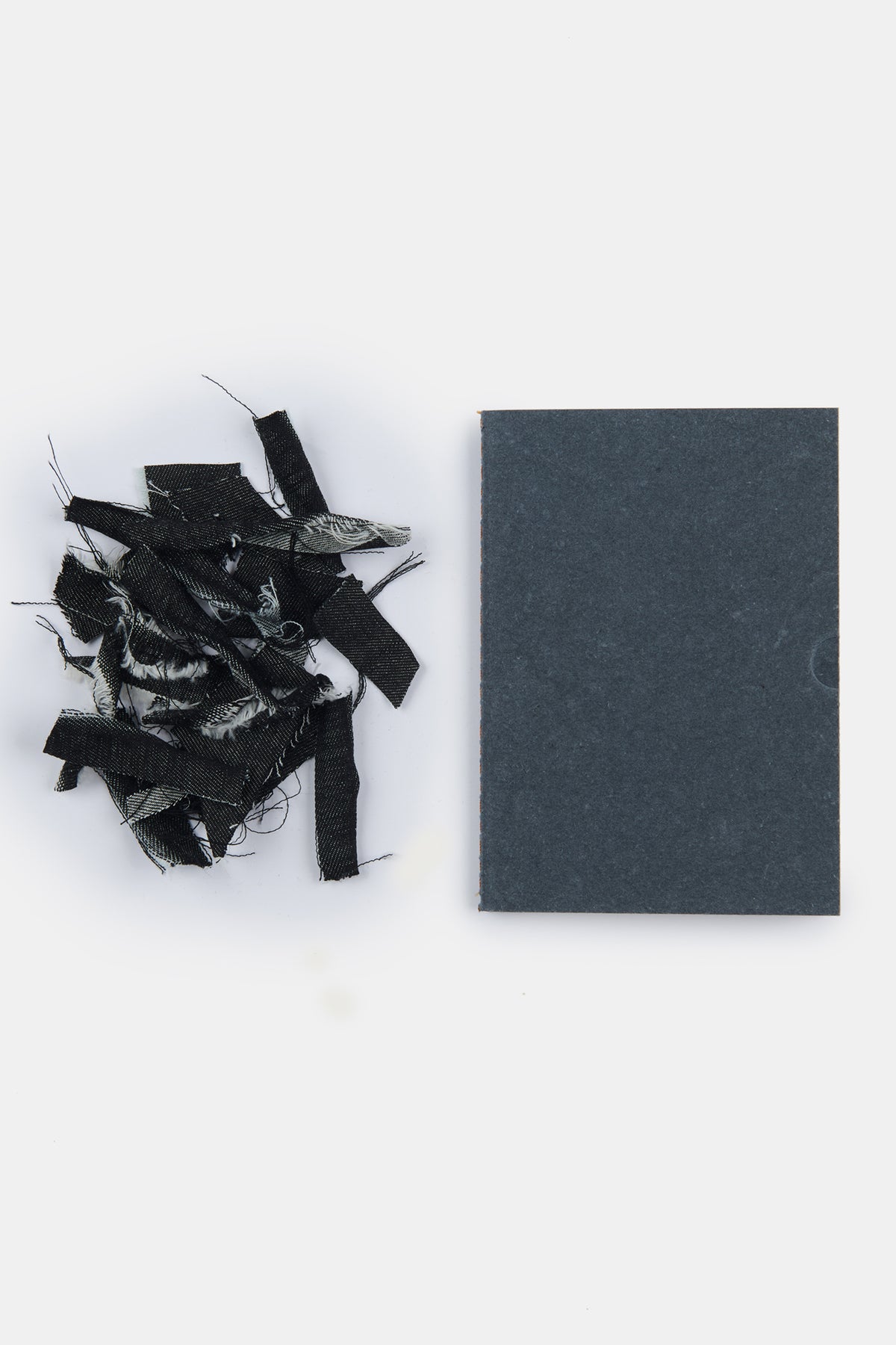 
            Flatlay of A6 Community Clothing X Mark + Fold notebook in black, next to a small pile of denim scraps to show what the notebook cover is made from. 