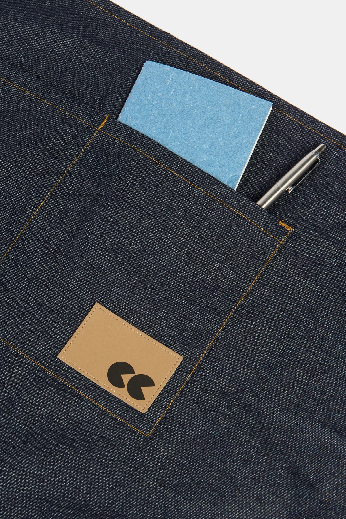 Community Clothing x Mark + Fold notebook in blue in the pocket of half apron in indigo with metal pen