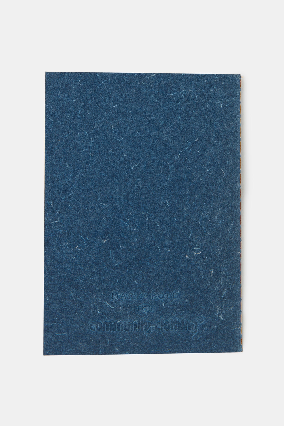 The back of A6 notebook with the Community Clothing x Mark + Fold logo embossed into the bottom.