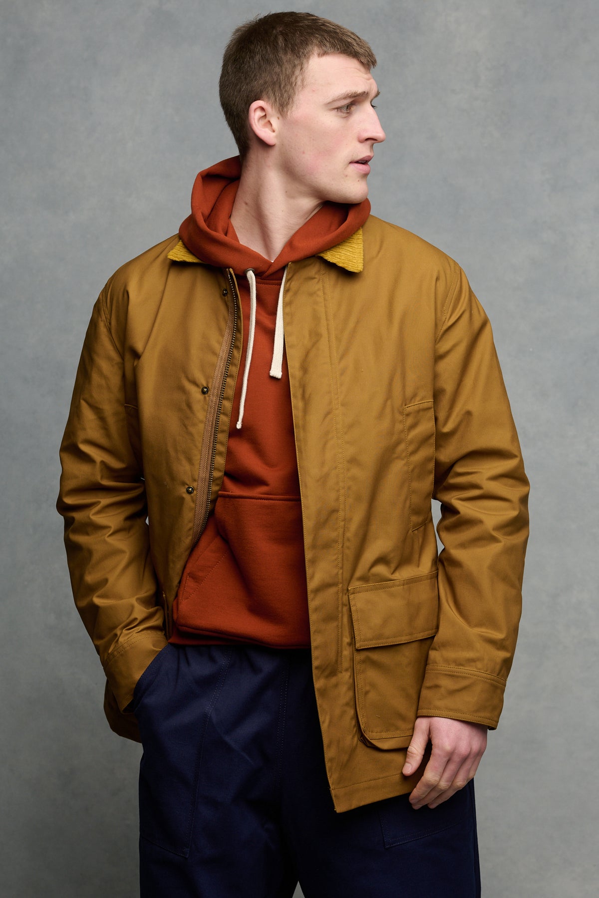 Thigh up image of men's car coat in dark tan unzipped over hooded sweatshirt in cinnamon