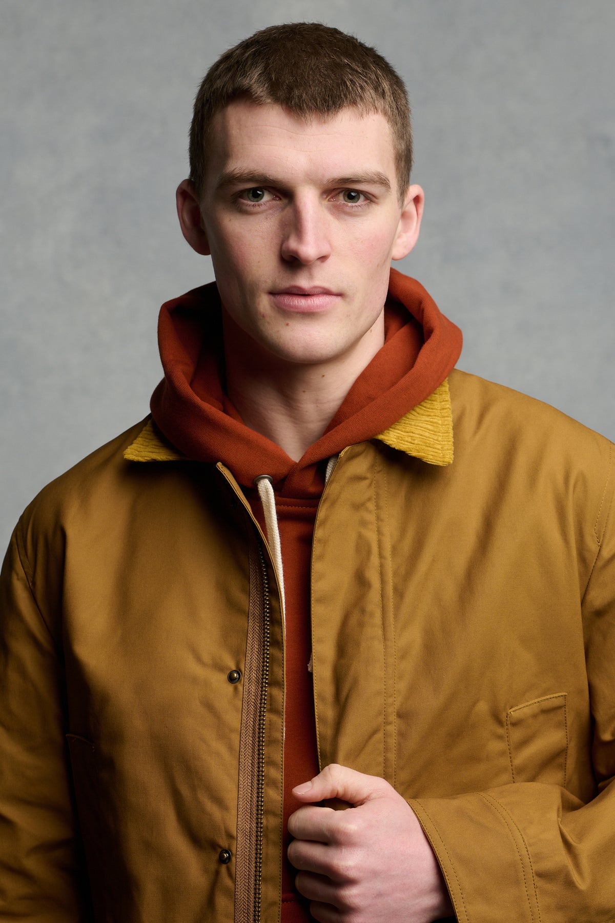 Portrait of male looking into the camera wearing men's car coat in dark tan with cord collar unzipped over cinnamon hooded sweatshirt