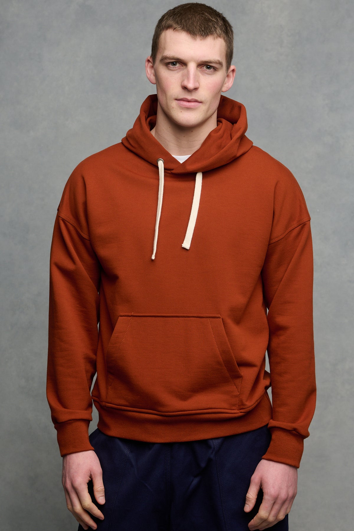 
            Thigh up image of male wearing hooded sweatshirt in cinnamon with one front pocket, worn over crew neck white t shirt