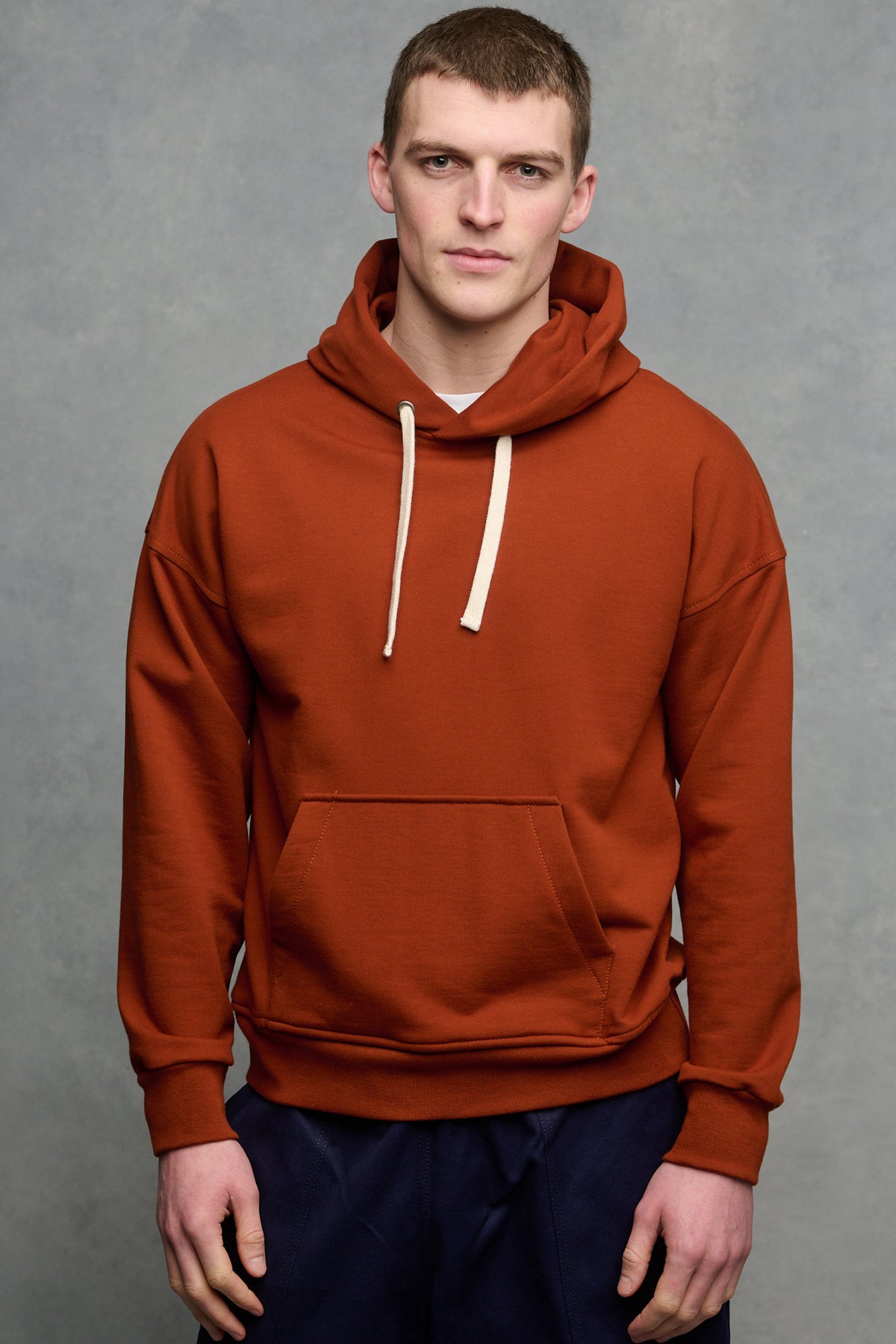 Thigh up image of male wearing hooded sweatshirt in cinnamon with one front pocket, worn over crew neck white t shirt