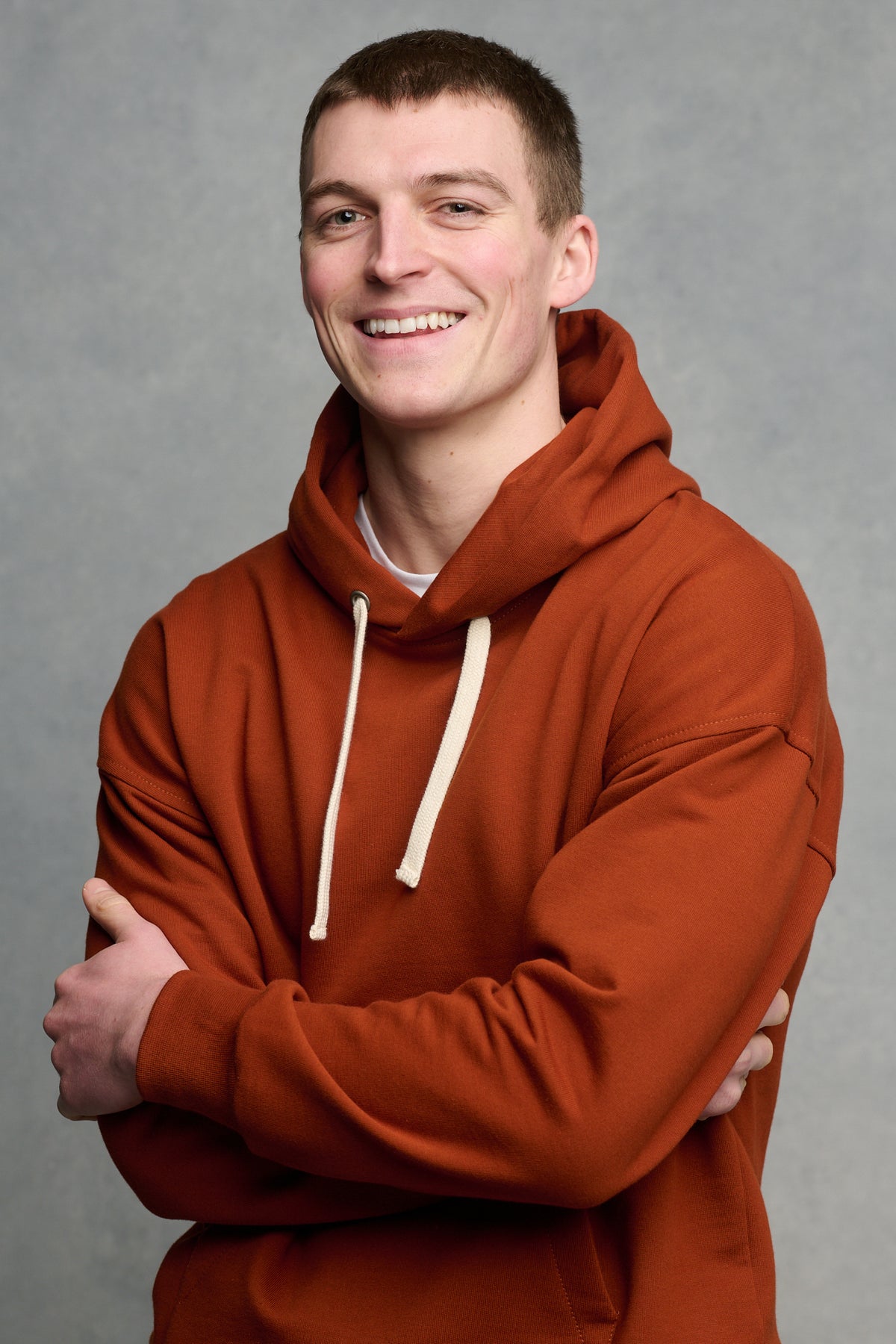 Hip up image of smiley male with his arms folded wearing hooded sweatshirt in cinnamon