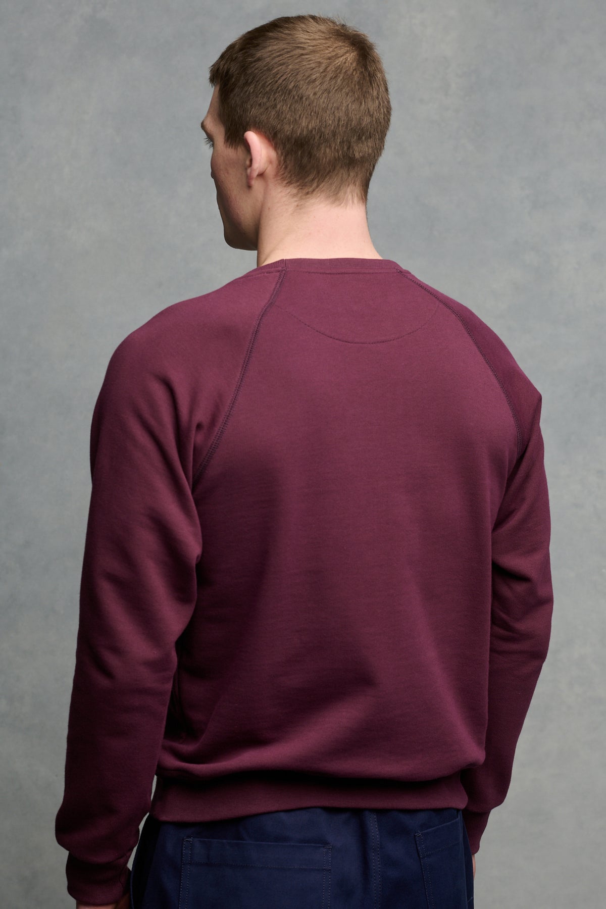 The back of brunet male wearing raglan sweatshirt in plum