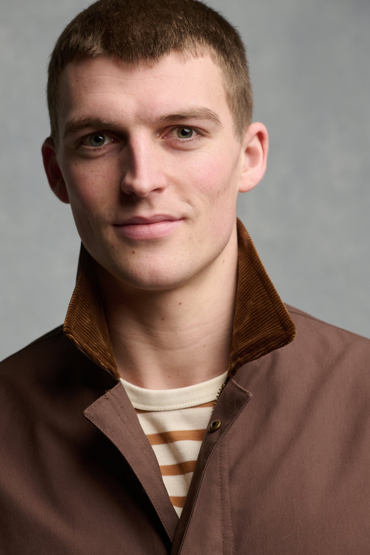 Portrait of brunet male wearing car coat in brown with brown cord collar up, worn over men's Breton in ecru cinnamon