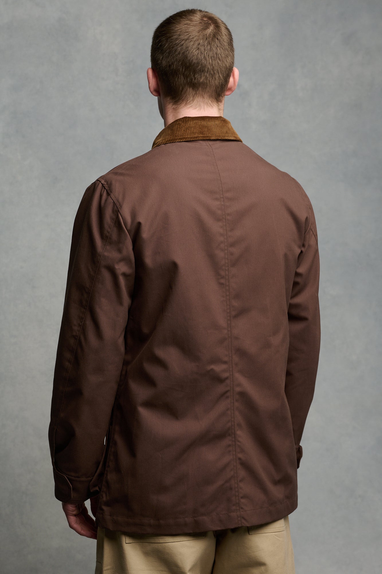 Thigh up image of male wearing men's car coat in brown unzipped over Breton in ecru cinnamon paired with cameraman pant in putty