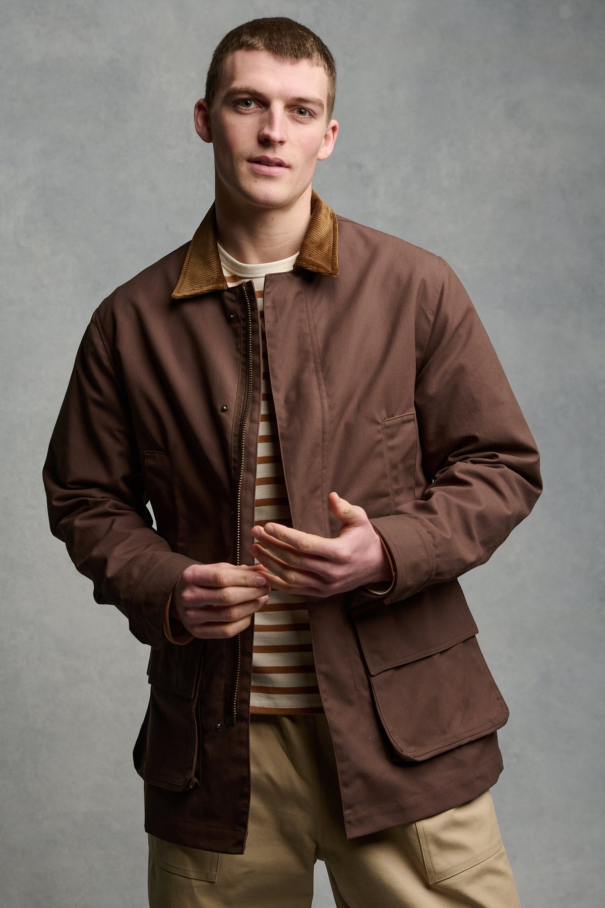 Thigh up image of men's car coat in brown unzipped over men's Breton in ecru cinnamon