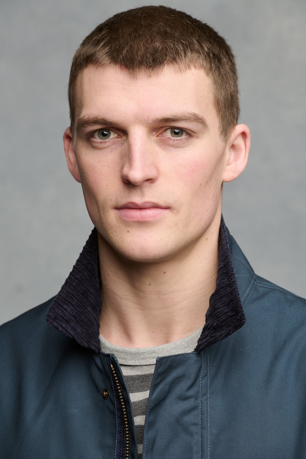 
            Close up portrait of brunet male with green eyes wearing unzipped car coat in navy with cord collar turned up.