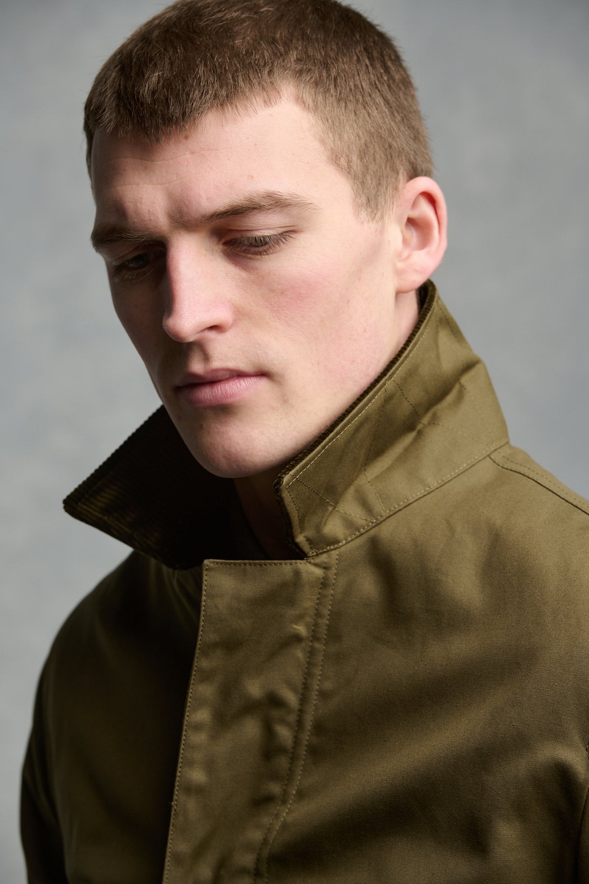 
            Close up portrait of brunet male wearing car coat in olive with cord collar up 