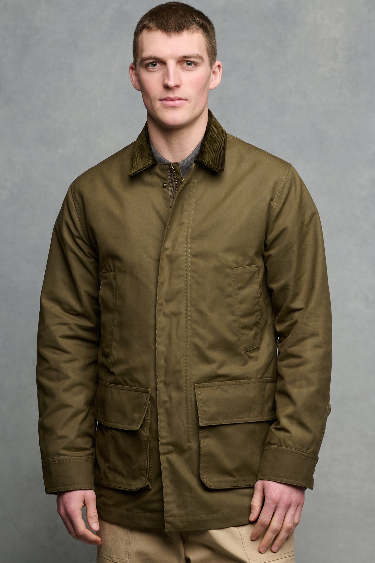 
            Thigh up image of brunet male wearing zipped and buttoned car coat with four front pockets.