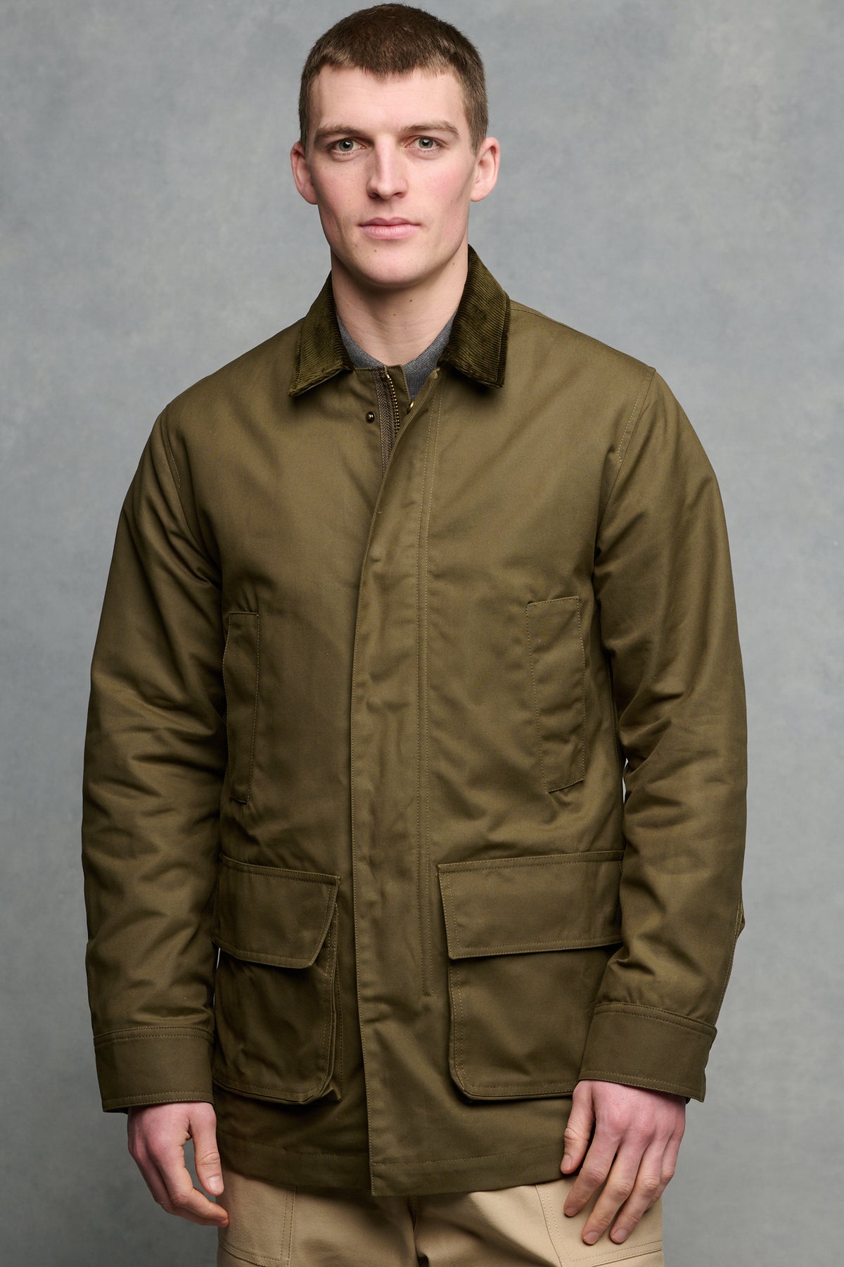 Thigh up image of brunet male wearing zipped and buttoned car coat with four front pockets.