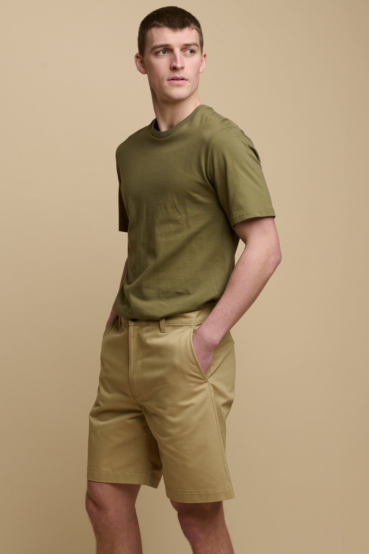 Calf up image of brunet male wearing men's classic shorts in stone with hands in front pockets