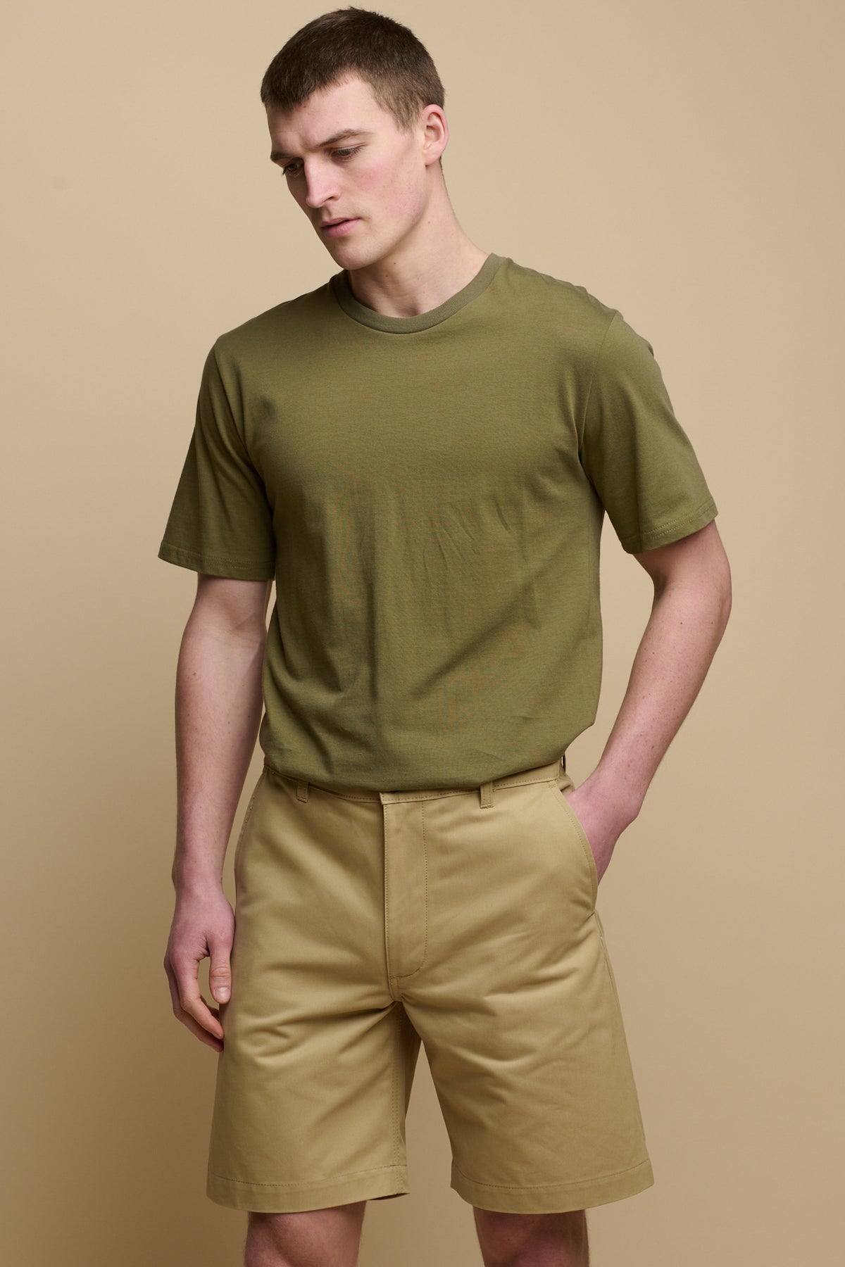 Thigh up front facing image of male wearing classic shorts in stone with hand in one of the front pocket and short sleeve t-shirt in olive tucked in