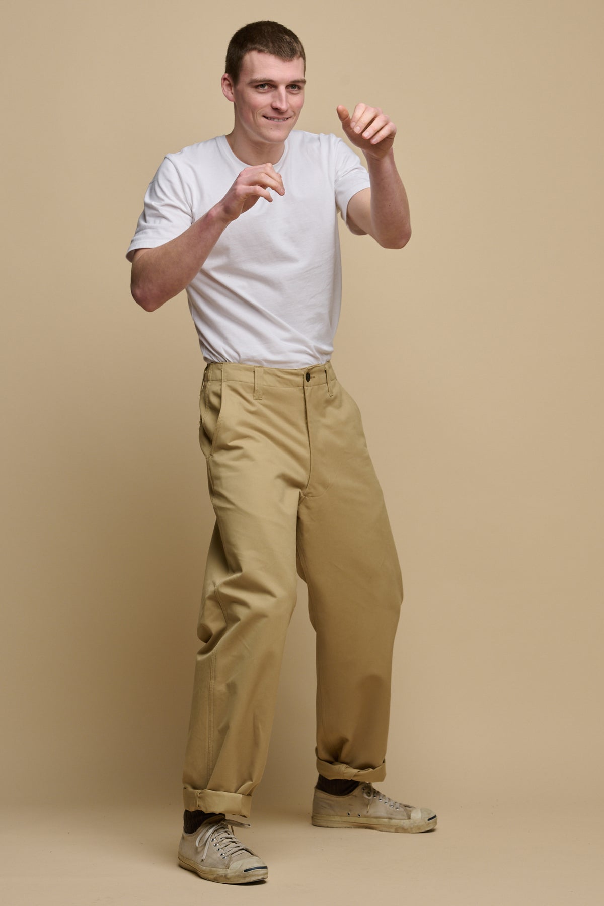 
            Full body action shot image of male punching the air wearing short sleeve t shirt in white tucked in field trousers in stone