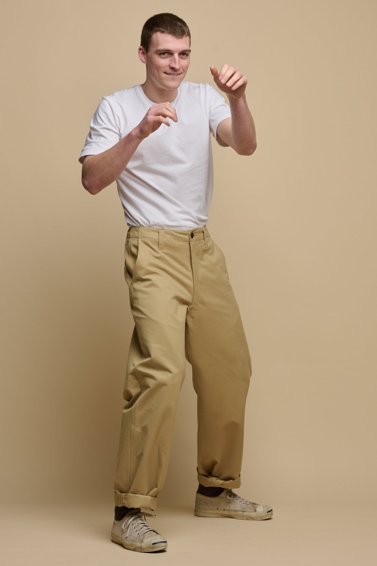 Full body action shot image of male punching the air wearing short sleeve t shirt in white tucked in field trousers in stone