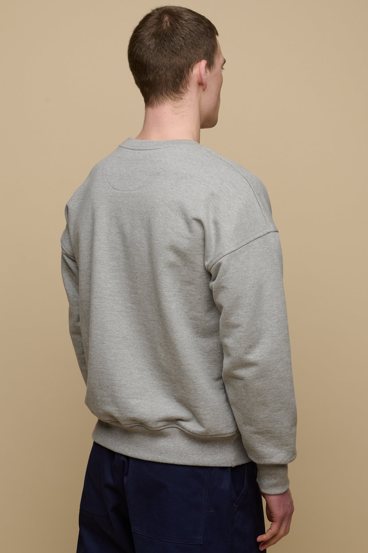 
            Thigh up back of brunet male wearing men&#39;s heritage drop shoulder sweatshirt in grey, paired with cameraman pants in navy