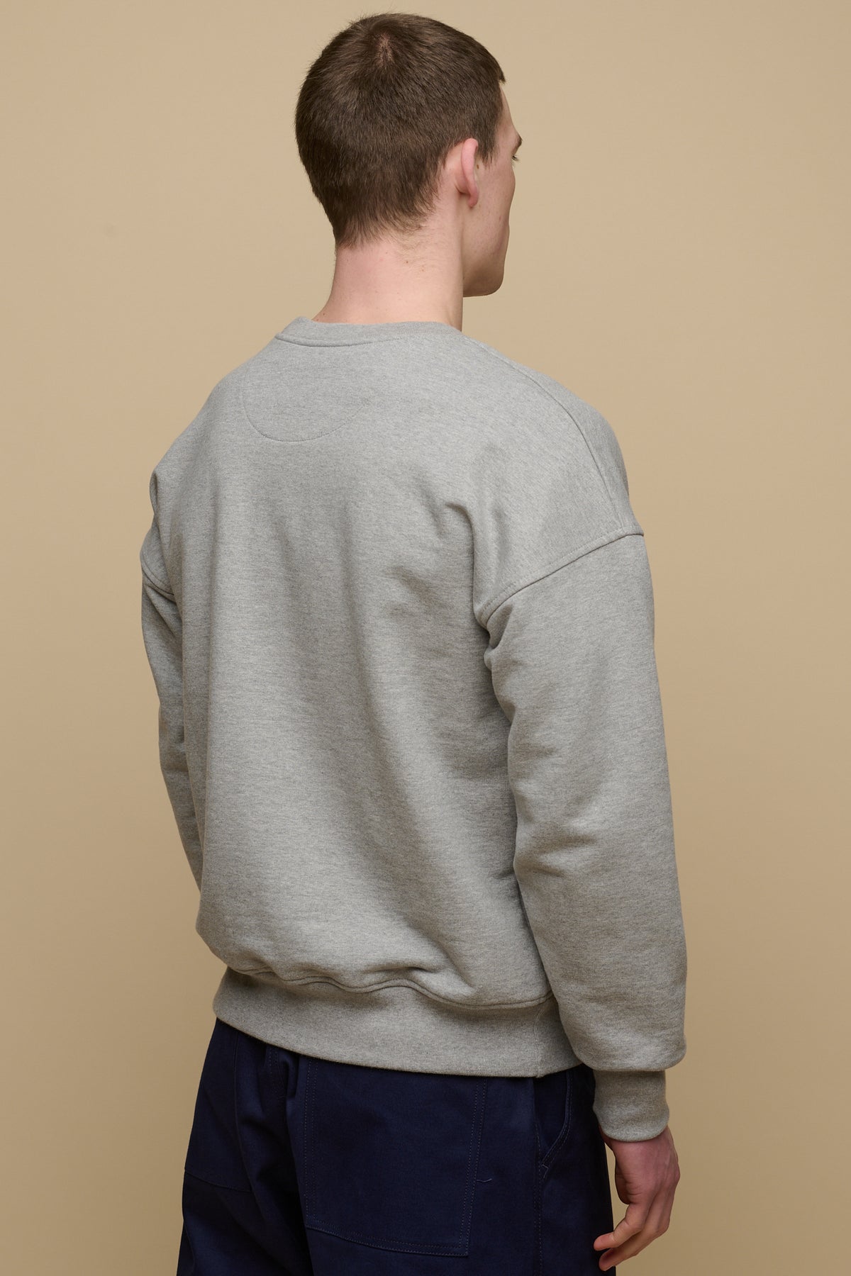 Thigh up back of brunet male wearing men's heritage drop shoulder sweatshirt in grey, paired with cameraman pants in navy