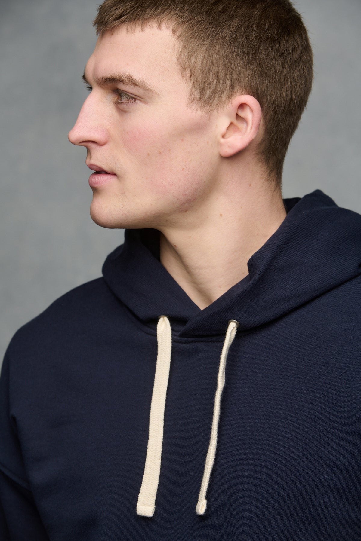 Thigh up image of male wearing hooded sweatshirt in navy with ecru drawstring through the hood