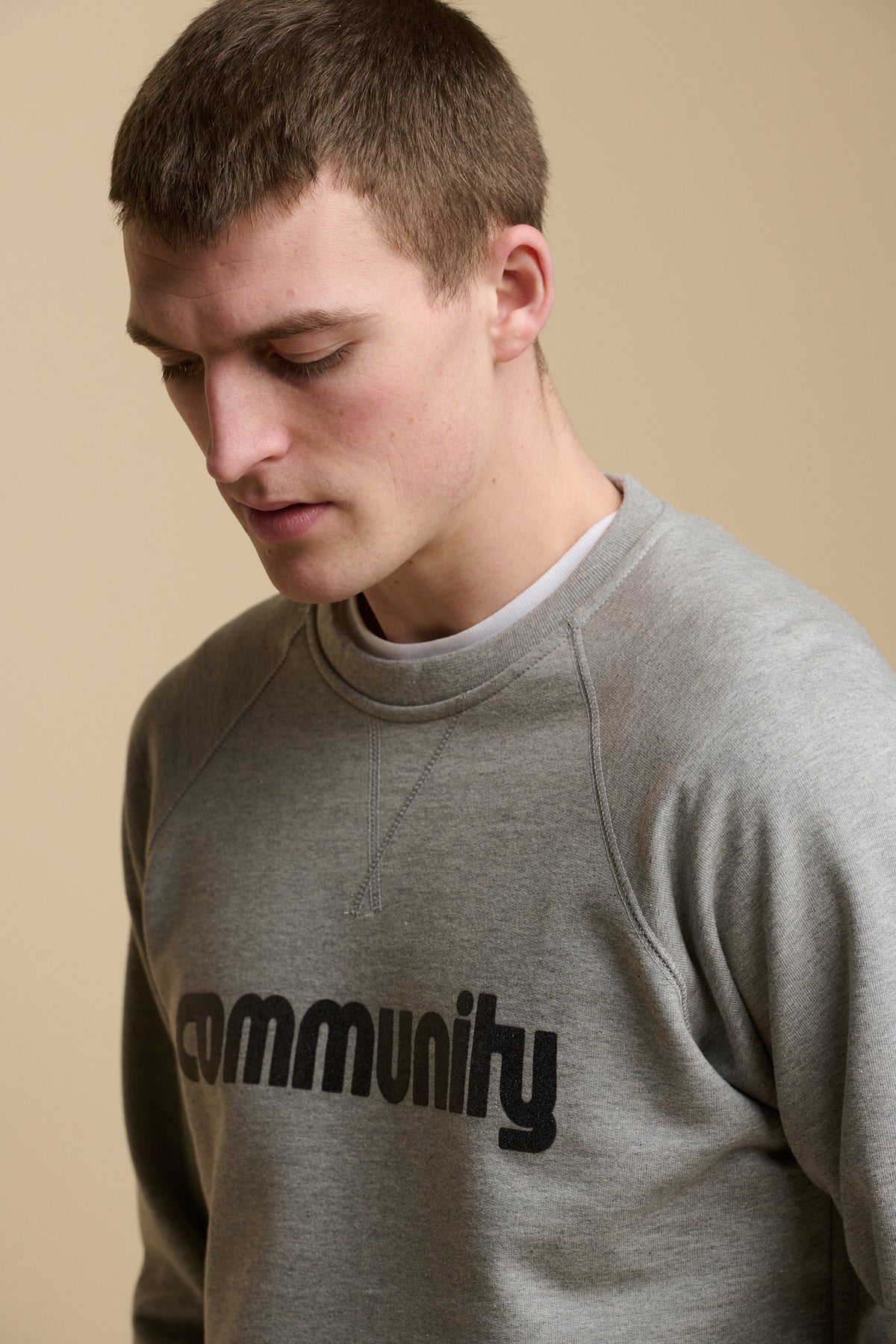 
            Portrait of male wearing logo raglan sweatshirt in grey marl with community logo across the chest