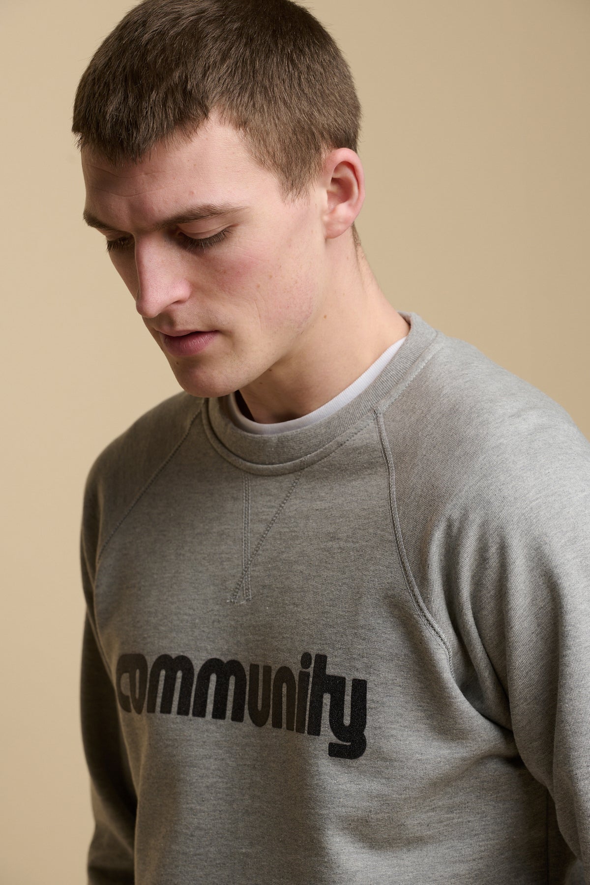 Portrait of male wearing logo raglan sweatshirt in grey marl with community logo across the chest