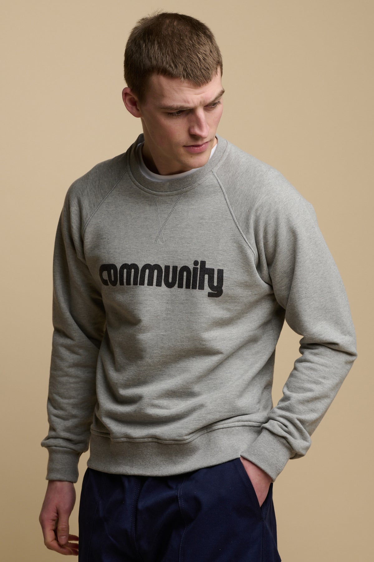 Thigh up image of male wearing Community logo across the chest of raglan sweatshirt in grey