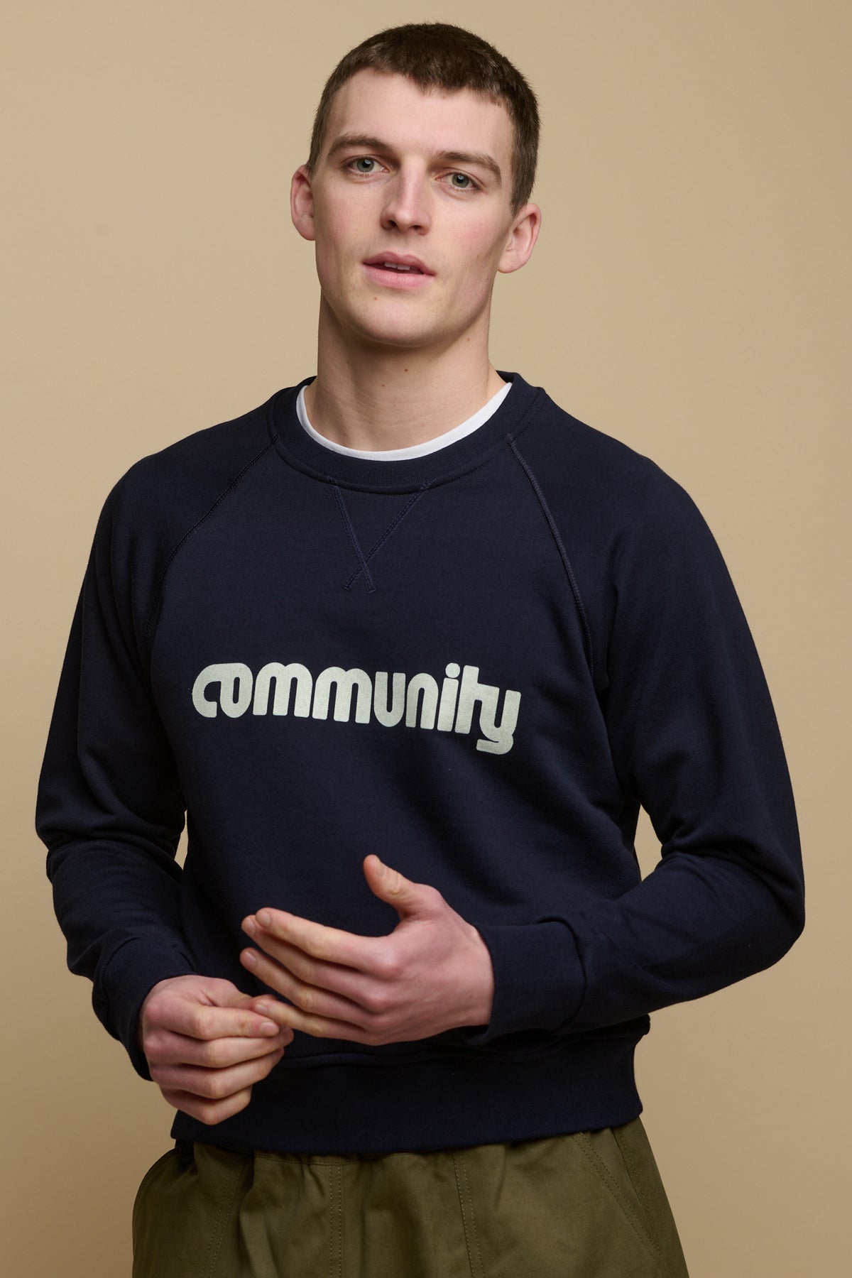 Hip up image of male wearing men's logo raglan sweatshirt in navy with white Community logo