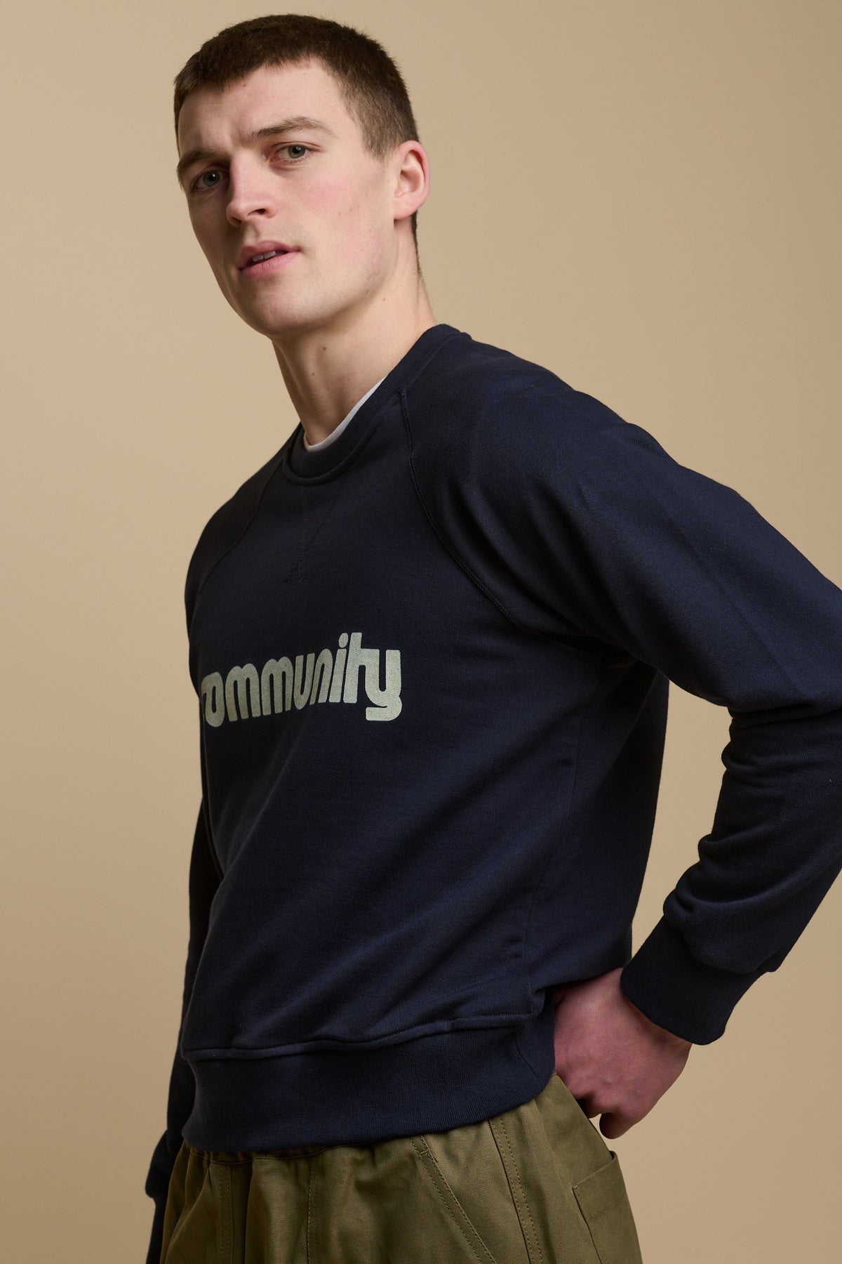 
            Thigh up image of male wearing men&#39;s raglan sweatshirt in navy with white Community logo across the chest