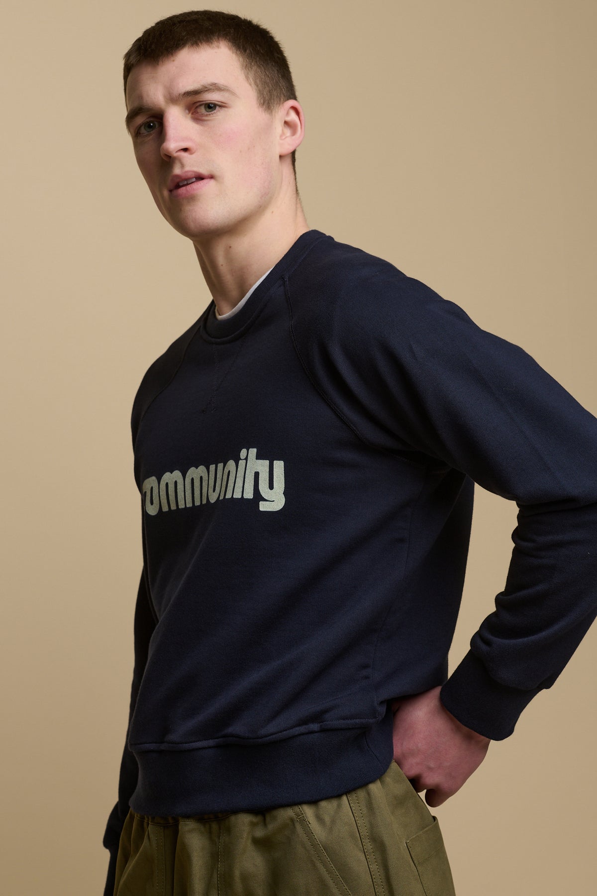 Thigh up image of male wearing men's raglan sweatshirt in navy with white Community logo across the chest