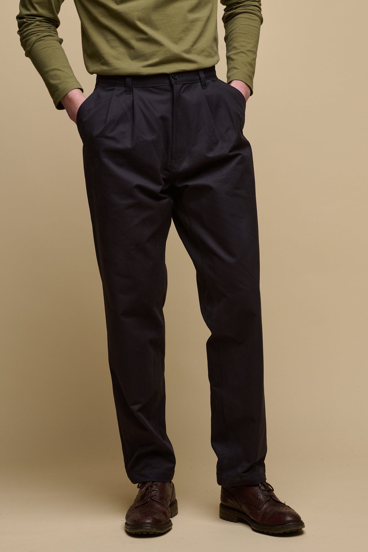 Chest down image of male wearing pleated cotton chino in navy with hands in front pockets