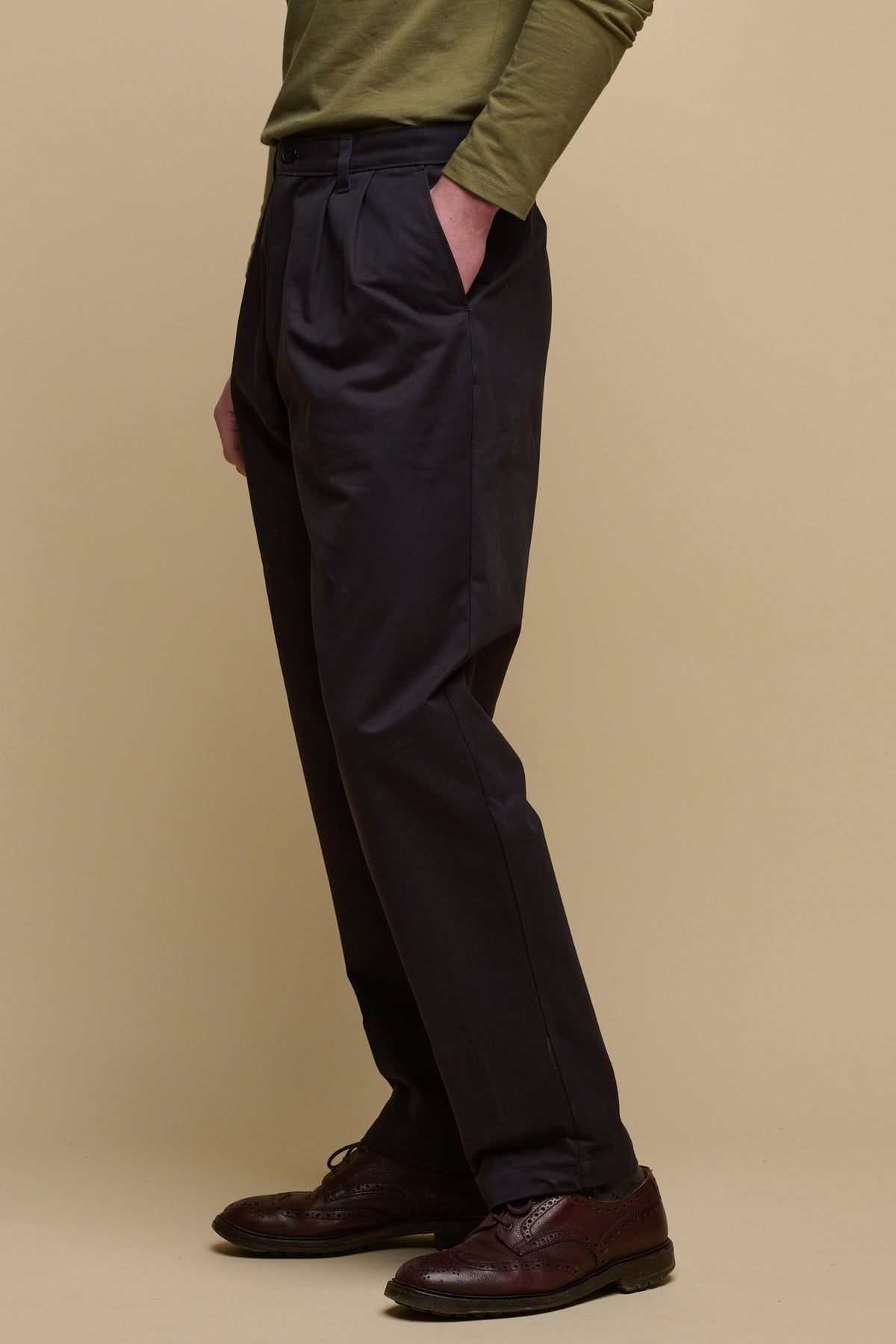 Waist down image of male wearing pleated cotton chino in navy with hand in front pocket, paired with brown leather shoes