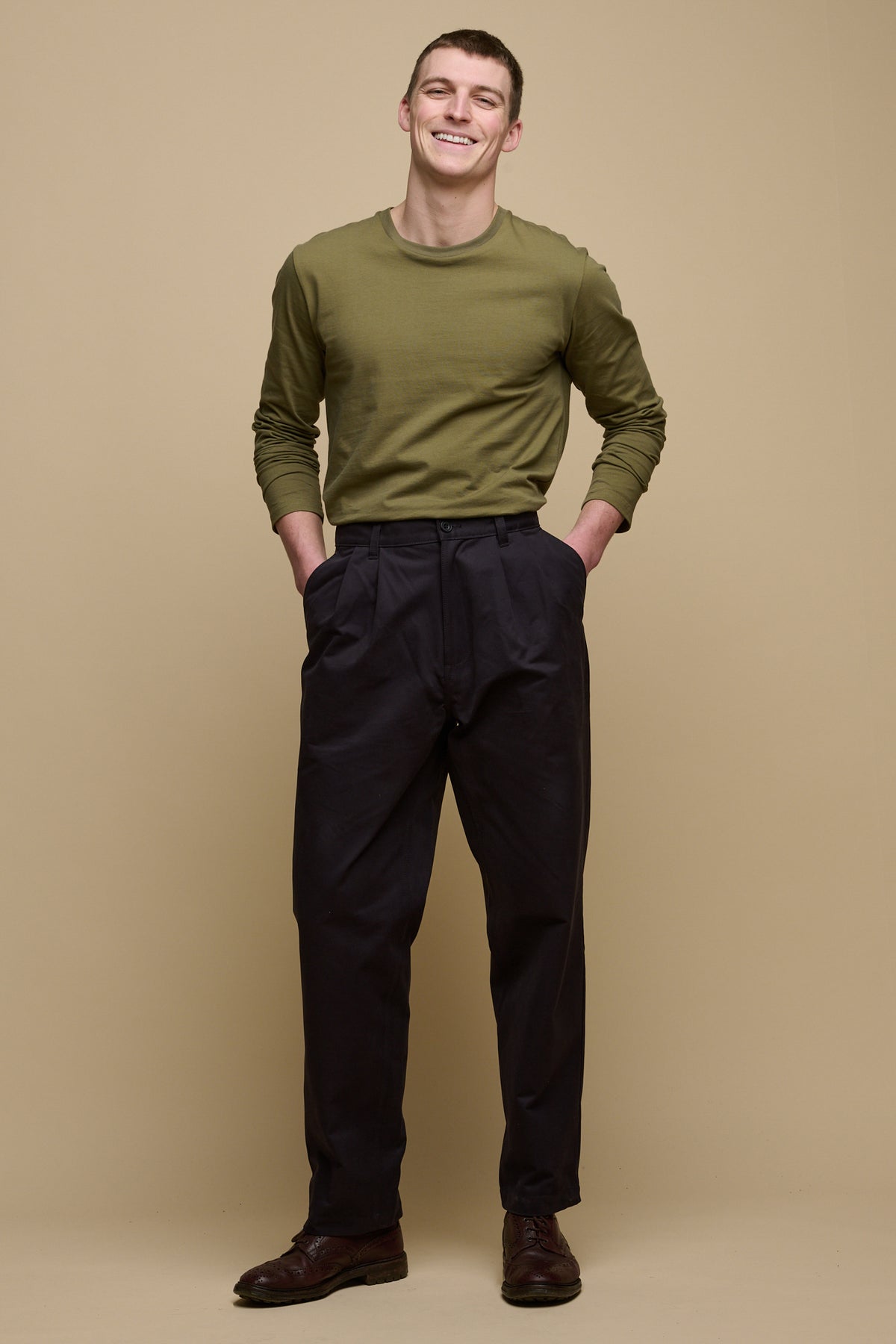 
            Full body image of brunet male wearing pleated cotton chino in navy paired with long sleeve t shirt in olive