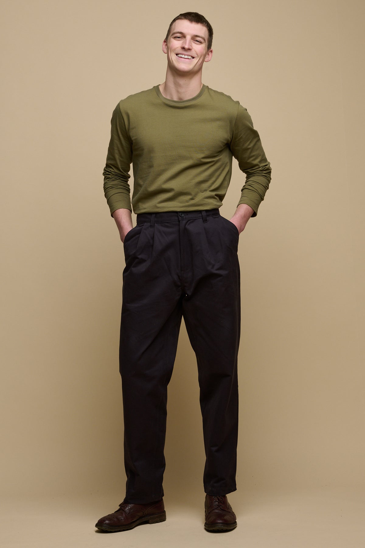 Full body image of brunet male wearing pleated cotton chino in navy paired with long sleeve t shirt in olive