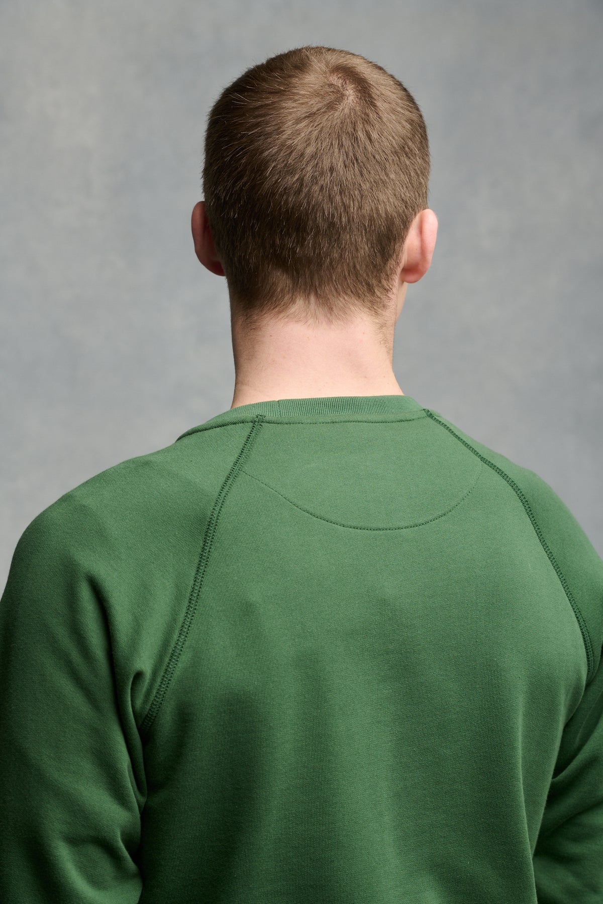 The back of male's shoulders wearing raglan sweatshirt in bottle green