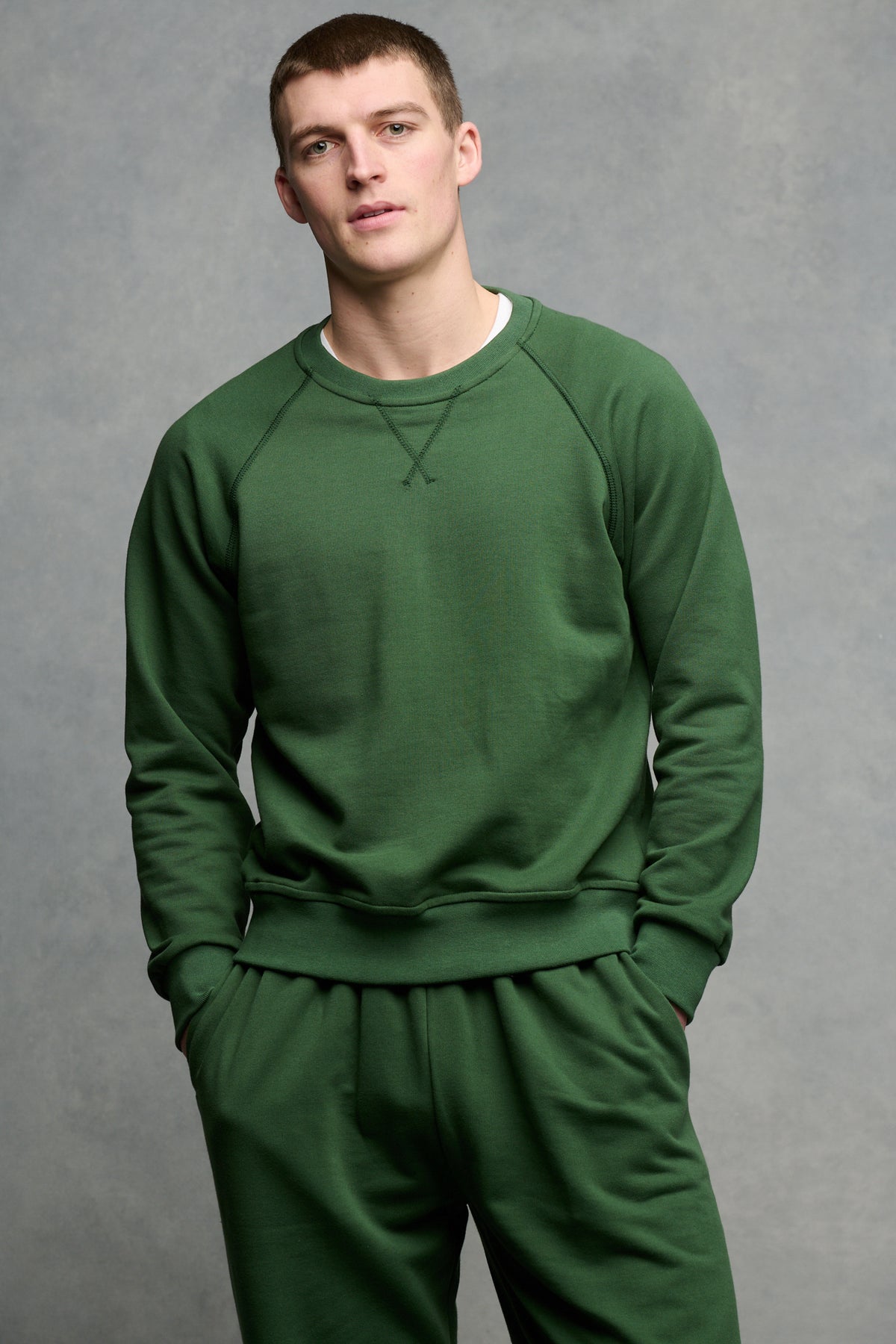 Thigh up front of male wearing raglan sweatshirt in bottle green with hands in front pocket of matching mens sweatpant in bottle green