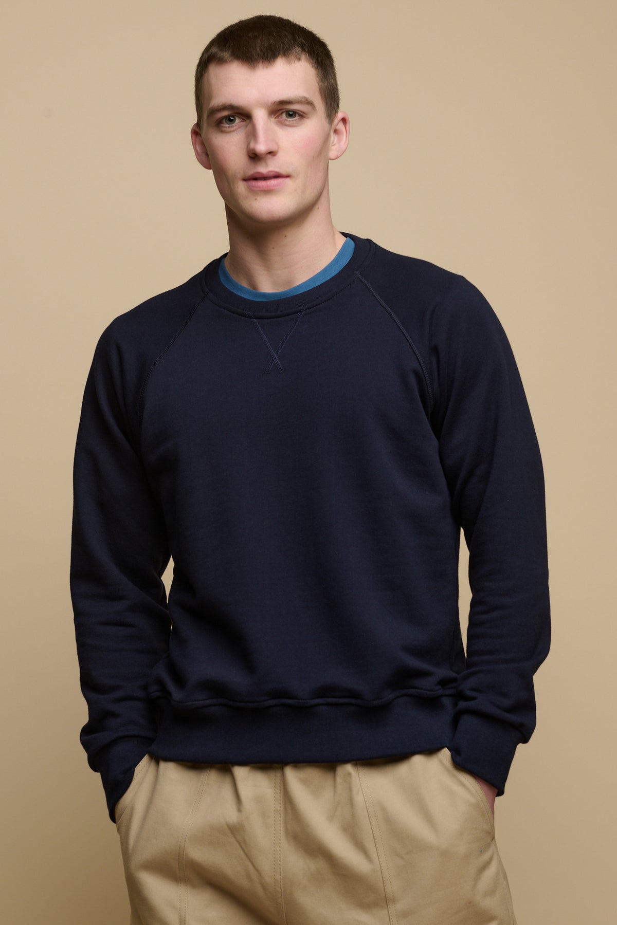 Thigh up image of brunet male wearing raglan sweatshirt in navy worn over RAF blue crew neck t shirt
