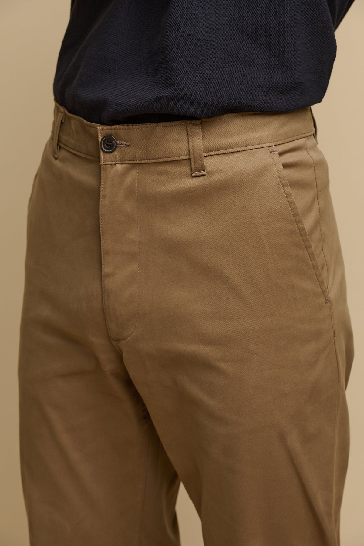 Close up shot of front of slim stretch chino in khaki, front pockets, zip fly and button fastening, belt loops on the waistband
