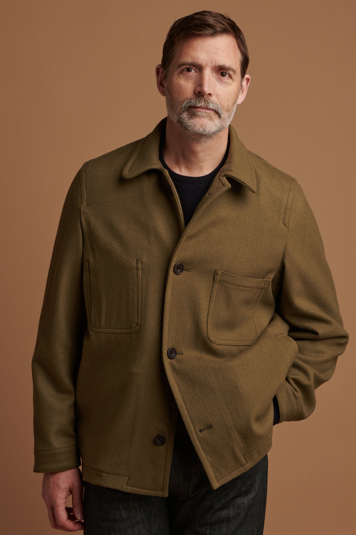 
            Patrick Grant facing the camera wearing Arthur wool chore jacket in olive with two out of four buttons fastened. Patrick wears the jacket over lambswool saddle shoulder crew neck in navy