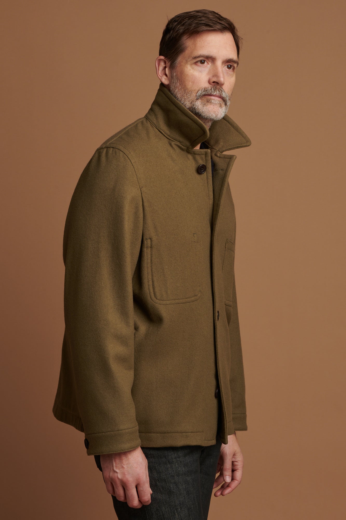 The side of Patrick wearing Arthur wool chore jacket in olive with the collar up. Four button fastenings down the front
