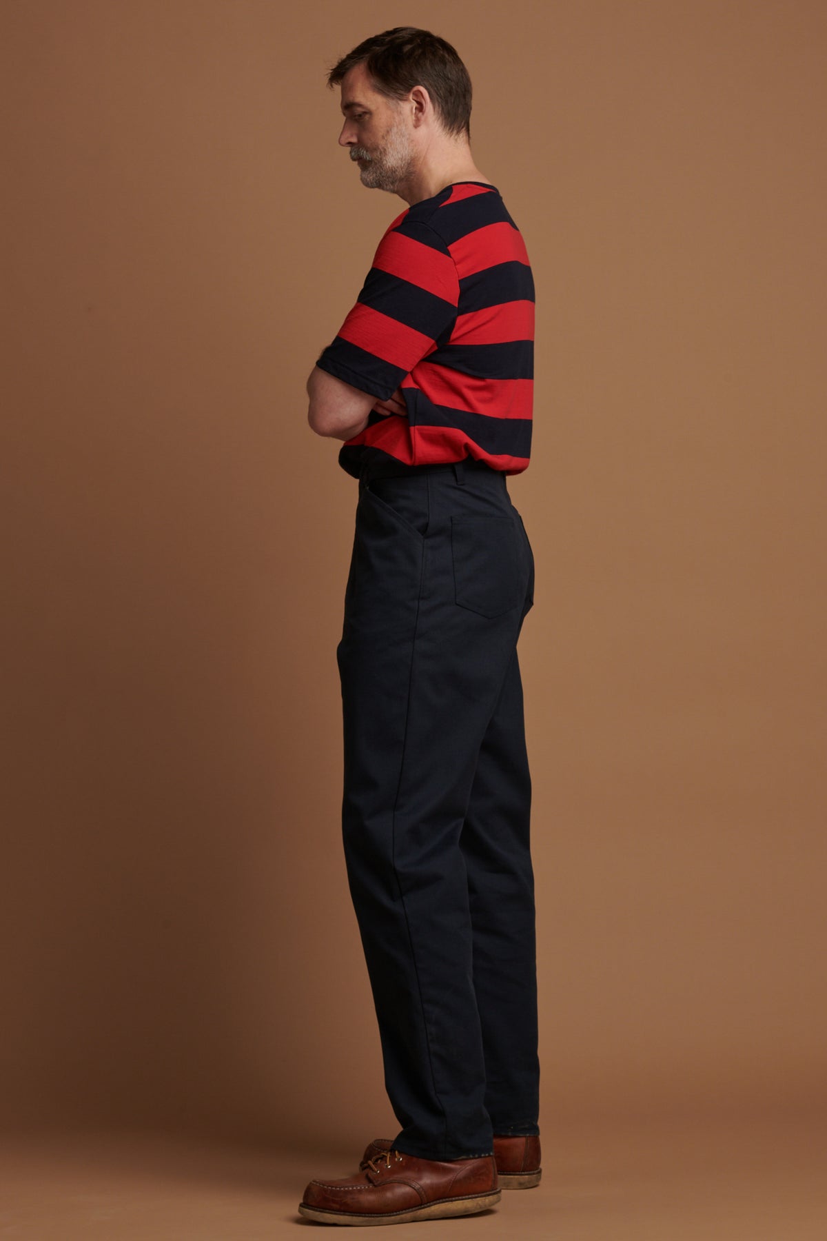 The left side of Patrick Grant canvas chore trousers in navy paired with wide stripe t shirt in red/navy tucked in.